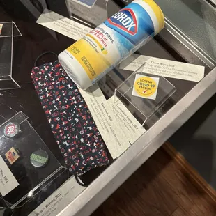 COVID masks, wipes, and vaccination stickers in a glass box alongside the timeline of Tulsa's history