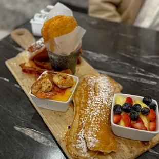 Small chef&apos;s board: French toast, bacon, hash browns, shrimp and grits, oblong pancakes stuffed with bacon, fruits
