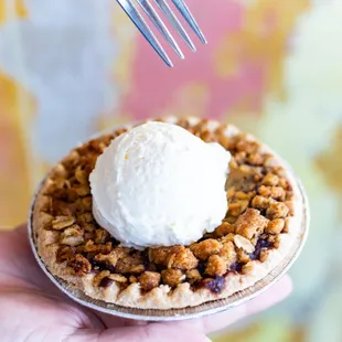 a hand holding a pie with a scoop of ice cream