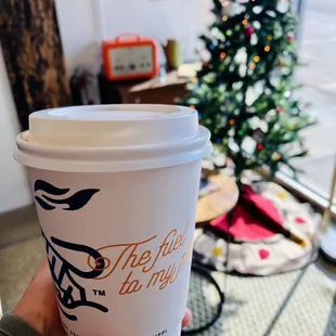 a person holding a coffee cup in front of a christmas tree