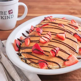 a plate of pancakes with strawberries and chocolate drizzle