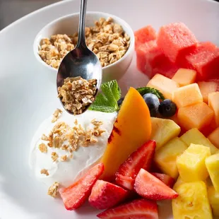 a plate of fruit with yogurt and granola