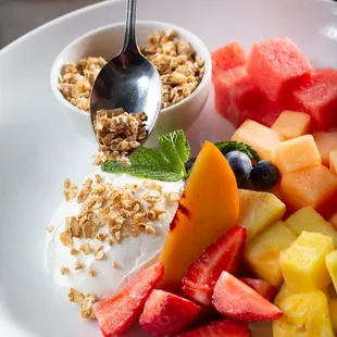 a plate of fruit with yogurt and granola
