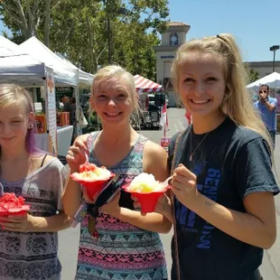 three girls holding cupcakes at an outdoor market