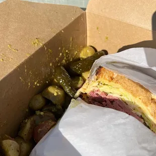 Reuben sandwich with potato salad and sweet pickles.