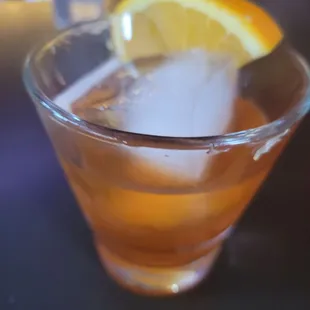 a drink in a glass with ice and a slice of orange