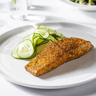 a fish fillet on a plate with cucumbers