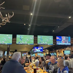 a group of people sitting at a bar watching sports on televisions