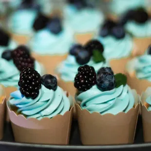 a variety of cupcakes with blue frosting and blackberries