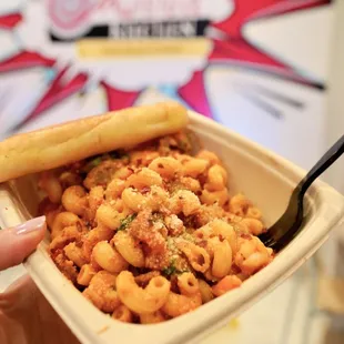 a hand holding a bowl of macaroni and cheese