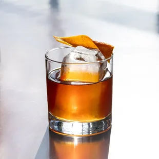 a glass of whiskey with an orange garnish