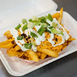 a container of fries with sour cream and green onions