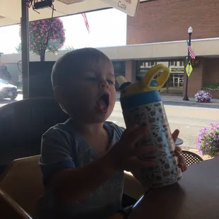 a young boy sitting at a table with a drink in his hand