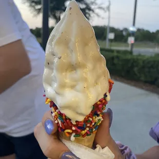 a person holding a cone of ice cream with sprinkles and sprinkles