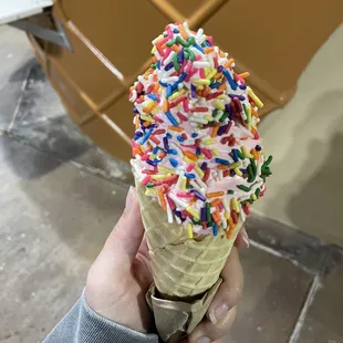a hand holding an ice cream cone with sprinkles
