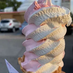 Small strawberry vanilla twisted soft serve in a waffle cone.