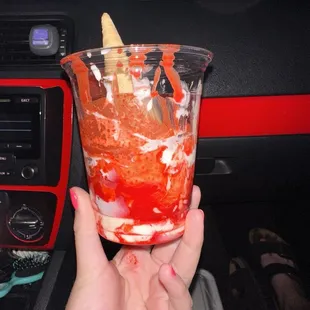 a hand holding a cup of ice cream and strawberries