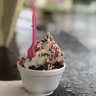 a cup of ice cream with sprinkles and a pink fork