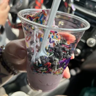a hand holding a cup of ice cream with sprinkles and sprinkles