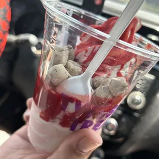 a hand holding a plastic cup filled with fruit and ice cream