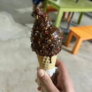 a hand holding an ice cream cone with sprinkles