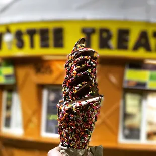 Chocolate dipped vanilla cone covered in rainbow sprinkles.