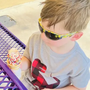 a young boy wearing sunglasses and eating an ice cream cone