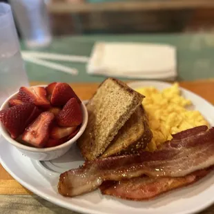 Cafe Breakfast with scrambled eggs, toast, bacon and fruit. The fruit cup had strawberries and bananas.