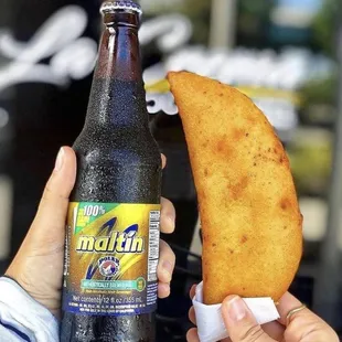 a person holding a beer and a piece of bread