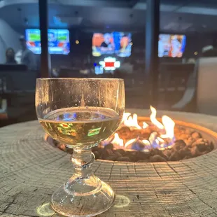 a glass of wine sitting on a table in front of a fire pit