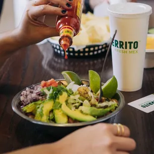 a person pouring ketchup on a plate of food