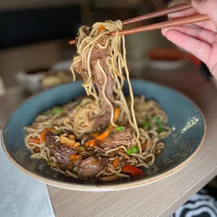 a person holding chopsticks over a bowl of noodles