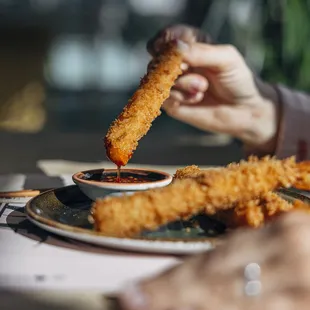 a person dipping a piece of deep fried chicken nuggies