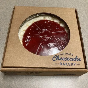 Medium cheesecake with strawberry topping, given in a cardboard box.