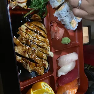a person holding a piece of sushi in a bento box