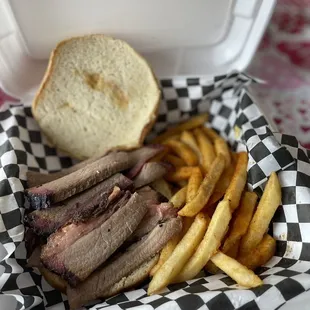 Sliced brisket sandwich with seasoned fries .