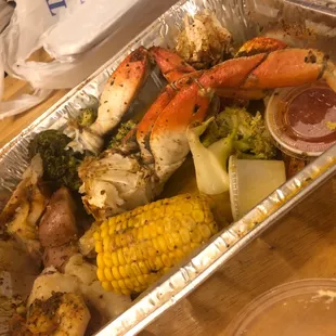 a tray of crab legs, potatoes, broccoli and corn