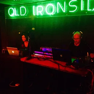two men sitting at a table in front of a neon sign