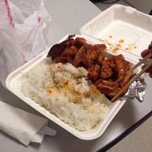 a takeout container with rice, meat and chopsticks