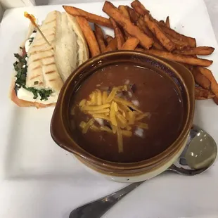 a bowl of chili soup with a sandwich and sweet potato wedges