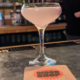 a pink cocktail with a sprig of rosemary