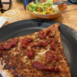 Slice of pizza with sun dried tomato and a side salad with spicy Thai dressing