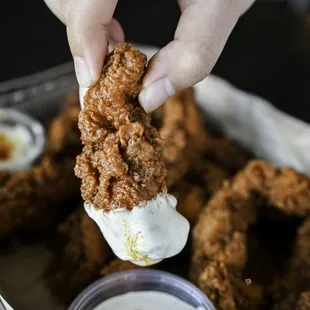 a hand dipping a fried onion ring