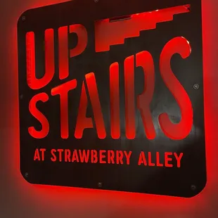 a sign that says upstairs at strawberry alley