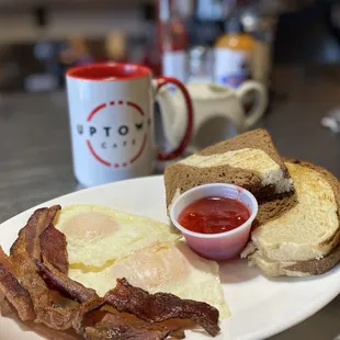Breakfast combo 3 with two eggs over medium, perfectly crispy bacon, homemade strawberry jam, and homemade rye bread.