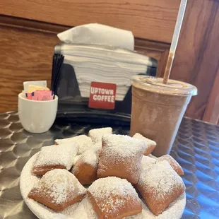 a plate of powdered sugared donuts and a cup of coffee