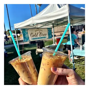 a hand holding two cups of iced coffee