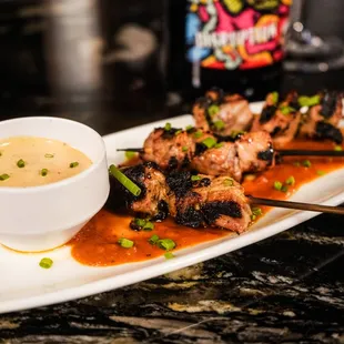 a plate of grilled chicken skewers and a bowl of sauce