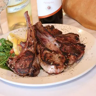 a plate of lamb chops and a bottle of wine