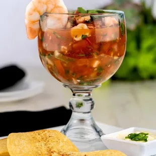 a glass of salsa with shrimp and tortillas